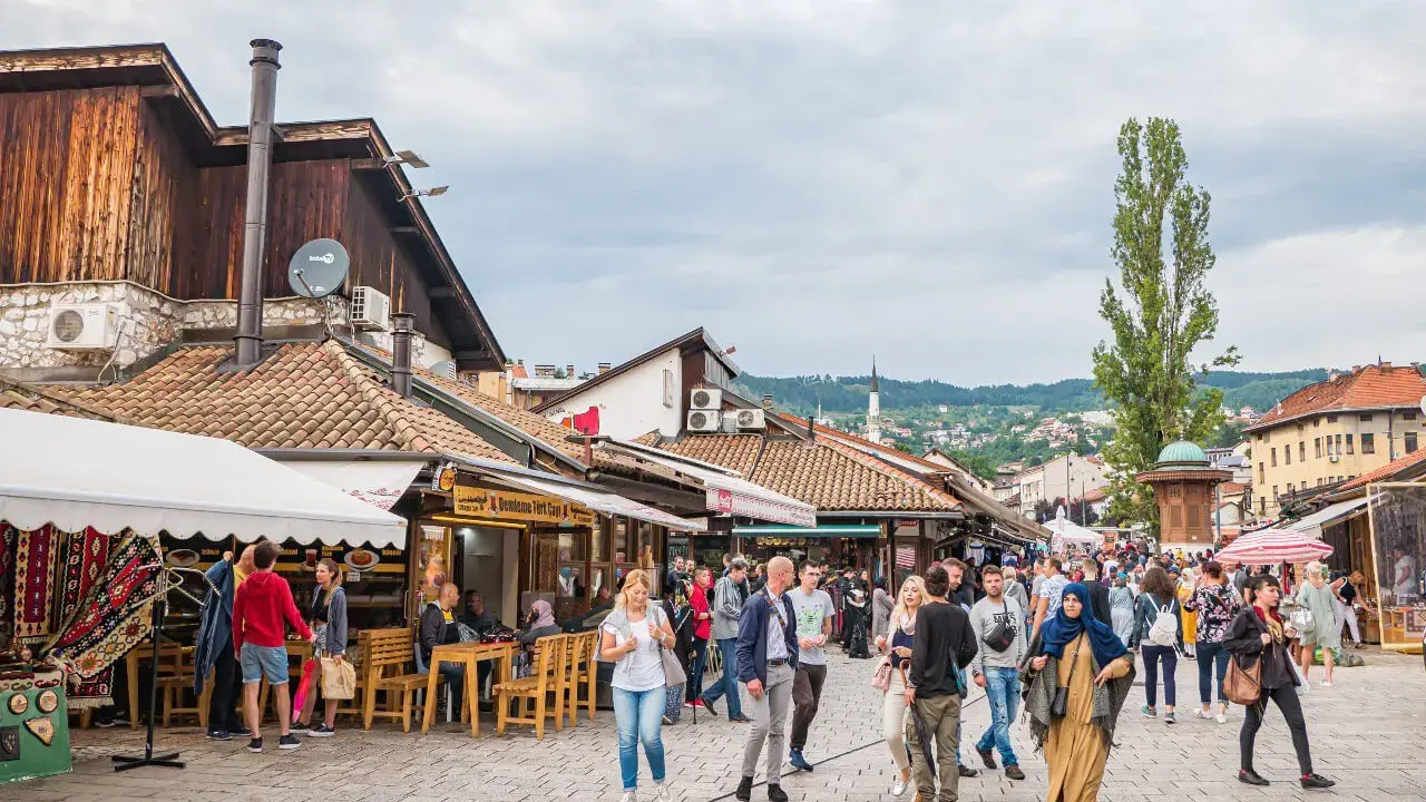 Tętniący życiem bazar w Bośni i Hercegowinie, z ludźmi spacerującymi między straganami i kawiarniami.