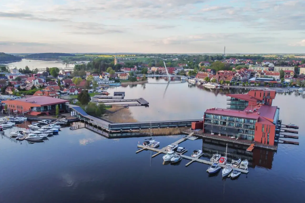 Nowoczesna marina i hotel na Mazurach. Widać tu liczne łodzie, nowoczesną architekturę i malowniczy krajobraz, idealne mazury atrakcje.
