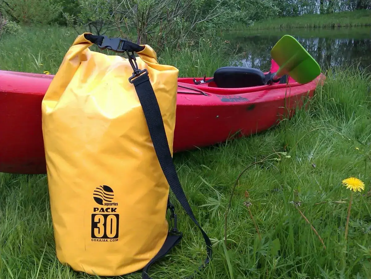 Żółta torba wodoszczelna Aquarius Pack 30 to idealny wybór, by wiedzieć, co zabrać na kajaki. Obok czerwony kajak i wiosło.