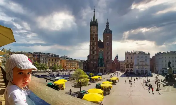 Małe dziecko w czapce z daszkiem patrzy na Rynek Główny w Krakowie. W tle Bazylika Mariacka i Sukiennice. Wspaniałe atrakcje dla dzieci Kraków.